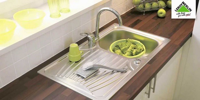 Νεροχύτης αλουμινίου με διάφορα μαγειρικά σκεύη, λαχανικά και φρούτα, πάνω σε καφέ πάγκο κουζίνας