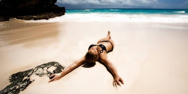 Καλλίγραμμη γυναίκα στην θάλασσα το καλοκαίρι αγνοώντας τις 4 απειλές για το δέρμα της:  άμμος, ήλιος, ζέστη,  χλώριο πισίνας