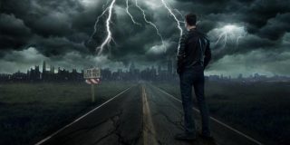 Άντρας στέκεται σε δρόμο που έχει κλείσει κοιτώντας ακραία καιρικά φαινόμενα (κεραυνοί - αστραπές) πάνω από μια μεγάλη πόλη