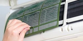 Χέρι ψυκτικού καθαρίζει τα φίλτρα σκόνης σε οικιακό κλιματιστικό τοίχου κατά την διάρκεια συντήρησης του air condition