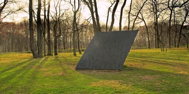 Γρανιτένια κατασκευή γλυπτό - μνημείο σε άλσος που παραπέμπει νοητά στο γεωμετρικό σχήμα Ρόμβος και στο εμβαδόν του