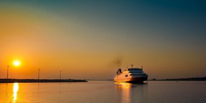 Πλοίο εισέρχεται κατά την δύση του ήλιου σε λιμάνι ● Φθηνά ακτοπλοϊκά εισιτήρια και δρομολόγια πλοίων